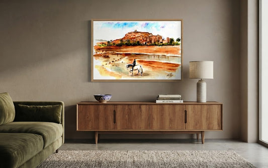 Tableau encadré de l'aquarelle « Le Cavalier de la Kasbah », accroché au mur au-dessus d'un meuble en bois bas dans un salon moderne aux teintes neutres.