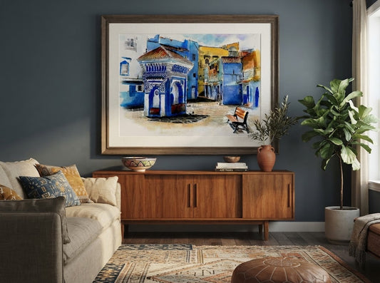 Tableau encadré de l'aquarelle « La Fontaine Bleue de Chefchaouen », accroché au mur au-dessus d'un meuble en bois dans un salon aux tons bleus et chaleureux.