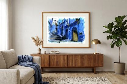 Aquarelle d'une ruelle de Chefchaouen, au Maroc, encadrée dans un bois chaud, suspendue au-dessus d'un buffet dans un salon