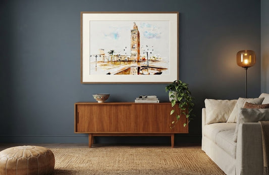 Tableau encadré de l'aquarelle « Regard sur la Koutoubia », accroché au mur au-dessus d'un meuble en bois dans un salon moderne aux tons bleus.
